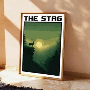 May include: A framed rectangular wall art print featuring a pixel art landscape of a stag standing on a cliff edge at sunset. The scene is rendered in shades of green and yellow, with the text THE STAG printed in black at the top of the white border.