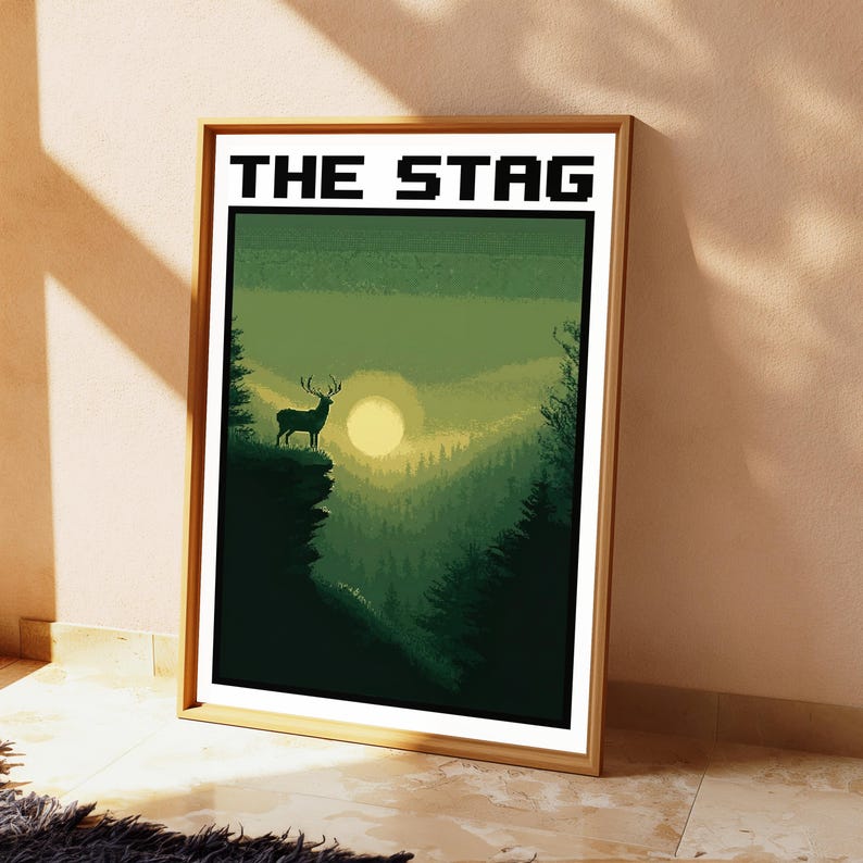 May include: A framed rectangular wall art print featuring a pixel art landscape of a stag standing on a cliff edge at sunset. The scene is rendered in shades of green and yellow, with the text THE STAG printed in black at the top of the white border.
