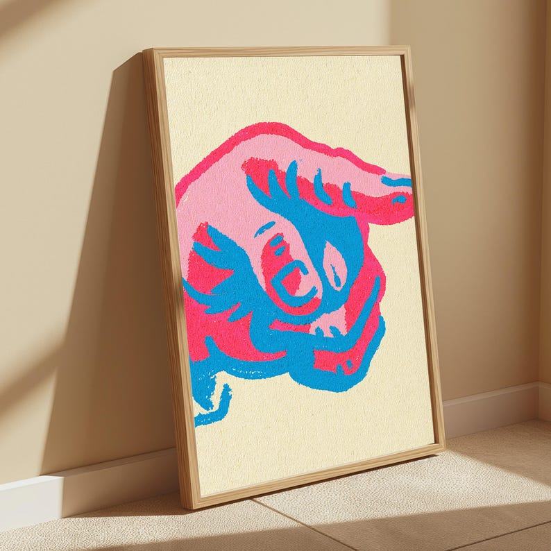 May include: A framed wall art print featuring a stylised, abstract illustration of a bull in vibrant shades of hot pink, light pink, and bright blue against a cream-coloured background. The artwork is encased in a simple, light-toned wooden frame.