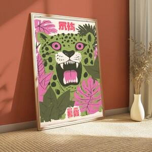 Peut inclure: Une impression d'art murale encadr&eacute;e repr&eacute;sentant un l&eacute;opard vert aux yeux roses, la gueule ouverte montrant les dents, entour&eacute; de feuilles tropicales roses et vert fonc&eacute;. L'impression comporte des caract&egrave;res chinois rouges en haut et en bas.