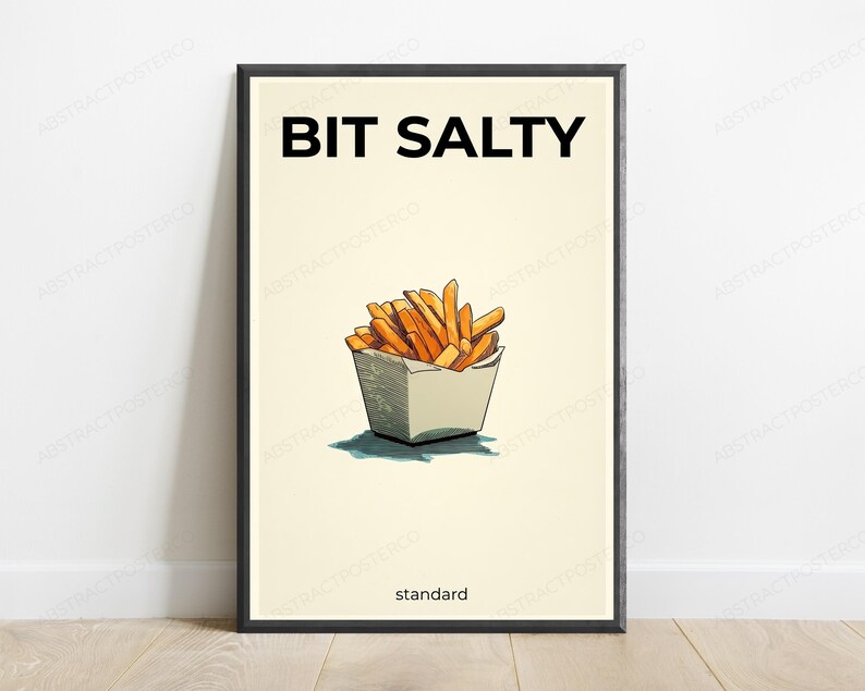 May include: A framed wall art print featuring a cream background with a black border. The text BIT SALTY appears in black at the top, and the word standard is at the bottom. A central illustration shows golden-brown french fries in a white container.