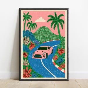 May include: A framed art print featuring a pink sports car driving along a winding blue road. The scene includes green palm trees, a dotted green mountain, and red and pink foliage against a pink sky with a single white cloud and a red-white kerb.