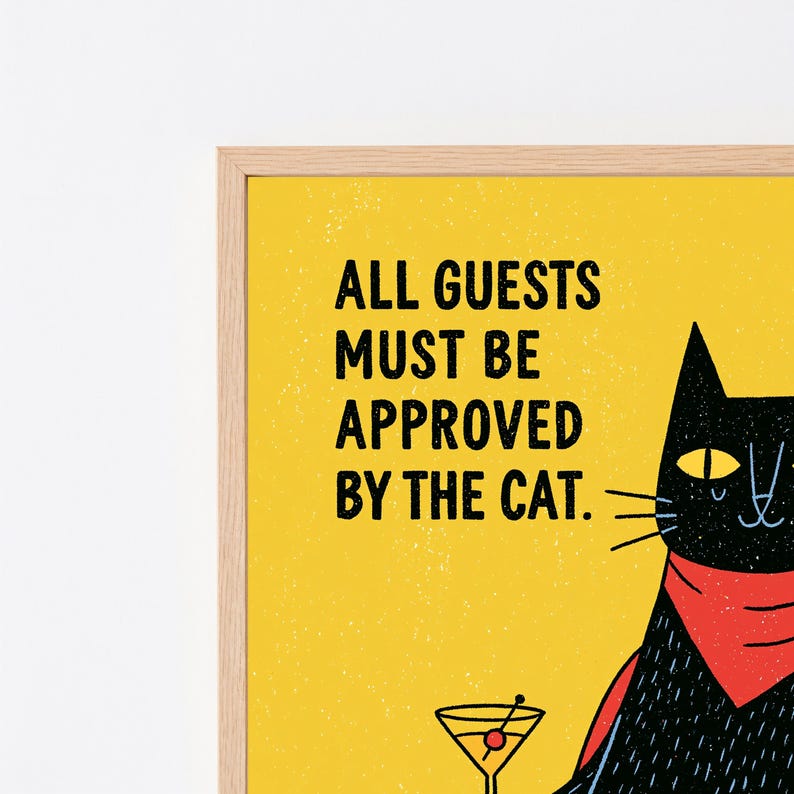 May include: A framed wall art print featuring a yellow background with the black text ALL GUESTS MUST BE APPROVED BY THE CAT. A black cat illustration wearing a red bandana is visible, holding a martini glass with a red olive inside the glass.