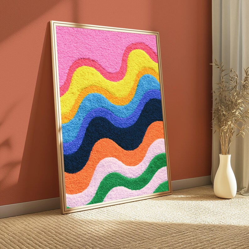 May include: A rectangular wall art piece in a thin gold frame featuring a textured, tufted surface with horizontal wavy bands of color. The design displays vibrant layers of pink, yellow, orange, blue, dark navy, and green in a repeating pattern.