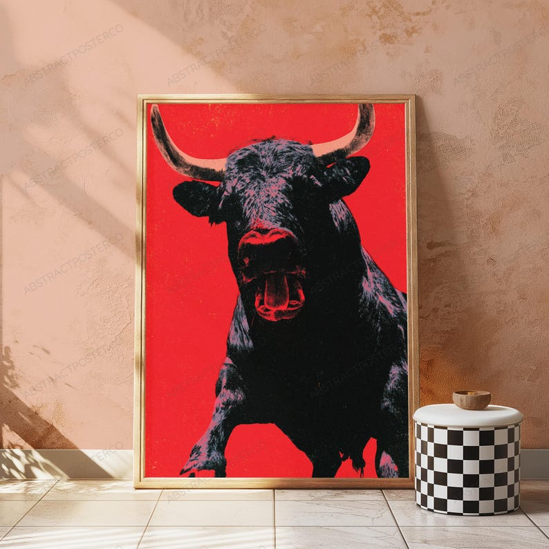 K&ouml;nnte beinhalten: Ein rechteckiger gerahmter Wandkunstdruck mit einer kontrastreichen Illustration eines Stiers mit dunklem Fell und markanten H&ouml;rnern vor einem einfarbigen, leuchtend roten Hintergrund. Der Stier ist frontal mit ge&ouml;ffnetem Maul dargestellt.