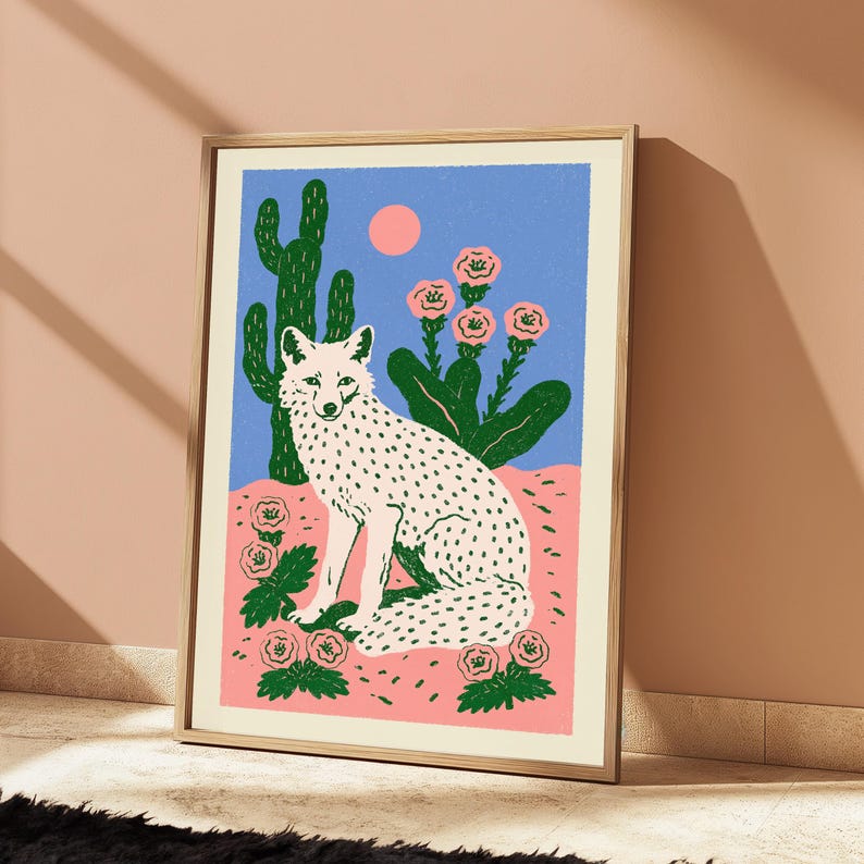Pu&ograve; includere: Una stampa artistica incorniciata raffigurante una volpe bianca con macchie nere seduta in un paesaggio desertico. La scena include un alto cactus verde, fiori rosa e un sole rosa pieno su un cielo blu, tutto in uno stile grafico piatto.