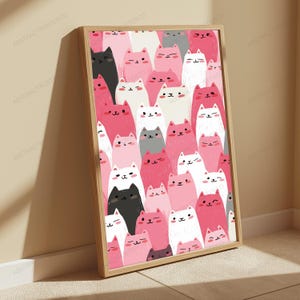 May include: A rectangular framed wall art print featuring a repeating pattern of cartoon cats in shades of pink, white, black, and gray. Each cat has a simple facial expression with eyes and a small mouth, arranged in a dense, overlapping vertical layout.