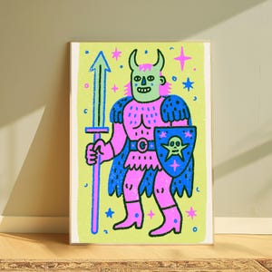 May include: A framed art print featuring a cartoon character with horns, wearing pink and blue armor, holding a blue sword and a blue shield with a skull emblem. The background is light green with scattered pink and blue stars and dots.