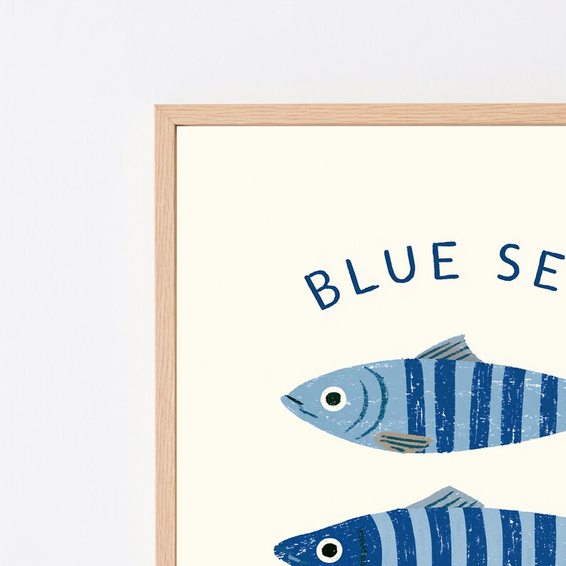 Pode incluir: Uma impress&atilde;o de arte emoldurada com dois peixes estilizados com listras verticais azuis e azul-claras sobre um fundo creme. O texto BLUE SEA est&aacute; impresso em letras mai&uacute;sculas azul-escuras acima dos peixes. A moldura &eacute; de madeira clara.