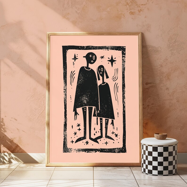 May include: A framed wall art print featuring a black ink illustration of two stylized figures standing side by side within a rectangular border on a light peach background, accented with small star shapes and curved line details throughout.