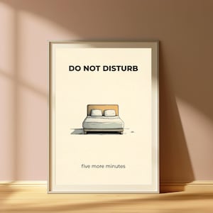 Puede incluir: Un cuadro enmarcado con las palabras "DO NOT DISTURB" sobre una ilustraci&oacute;n de una cama con dos almohadas. Debajo de la ilustraci&oacute;n de la cama, el texto dice "five more minutes". La obra de arte est&aacute; sobre un fondo crema.
