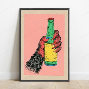 May include: A framed art print featuring a stylised illustration of a hairy, red-furred creature hand with sharp claws holding a green glass bottle with a yellow label against a solid pink background, enclosed in a simple black frame.