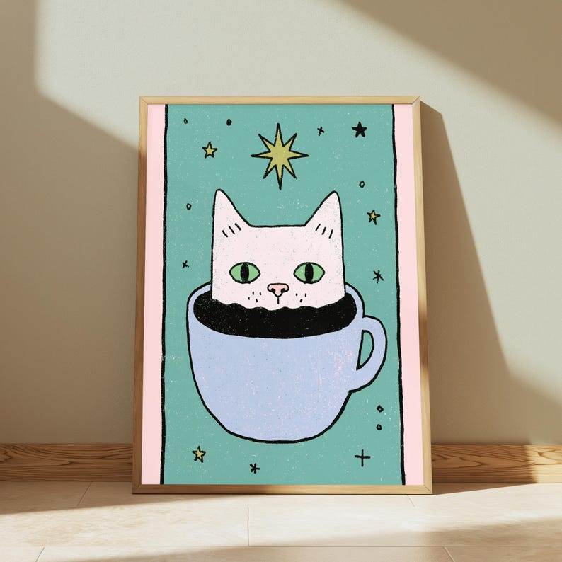 May include: A framed wall art print featuring a light pink cat with green eyes peeking out from a light blue coffee mug. The background is a teal rectangle with small yellow stars and black plus signs, bordered by vertical light pink stripes.