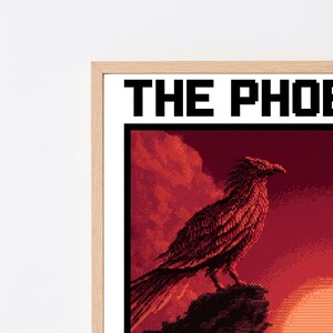 Puede incluir: Una impresi&oacute;n de arte en p&iacute;xeles enmarcada que muestra un p&aacute;jaro grande posado sobre una roca frente a un atardecer rojo intenso. El texto THE PHOE es visible en la parte superior con una fuente pixelada negra. El marco es de madera clara.