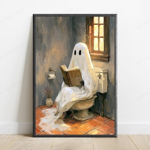 May include: A framed wall art print depicting a white ghost with black eyes sitting on a toilet in a bathroom, reading a brown book. The scene features orange tiled flooring, a window with warm light, and a toilet paper holder on the wall.