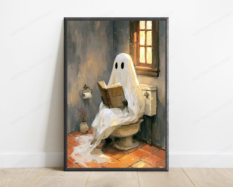 May include: A framed wall art print depicting a white ghost with black eyes sitting on a toilet in a bathroom, reading a brown book. The scene features orange tiled flooring, a window with warm light, and a toilet paper holder on the wall.