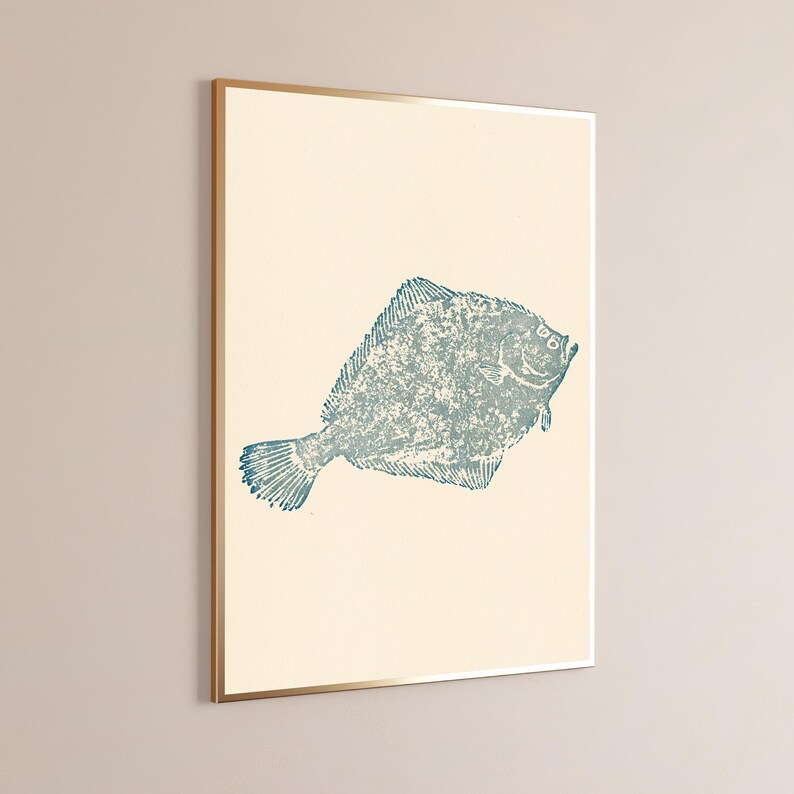 May include: A framed wall art print featuring a textured, blue-toned illustration of a flatfish centered on a solid, light cream-colored background. The artwork is enclosed in a thin, metallic gold frame, presenting a clean and simple aesthetic.