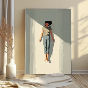 May include: A framed wall art print featuring a stylized illustration of a person with dark hair wearing a gray t-shirt and blue pants, floating in a vertical beam of light against a muted sage green background with sharp geometric shadows.