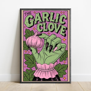 Pu&ograve; includere: Una stampa artistica incorniciata raffigurante una mano verde con lunghe unghie nere che tiene un bulbo d'aglio rosa. Lo sfondo &egrave; viola con foglie verdi e stelle arancioni. Il testo in alto recita THE GARLIC CLOVE in lettere verdi.