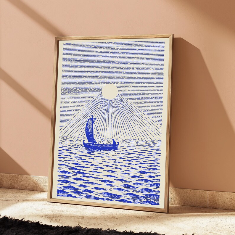 May include: A framed rectangular wall art print featuring a blue ink illustration on a cream background. The artwork depicts a small sailboat on a textured sea under a large sun with radiating lines that extend across the entire upper portion.