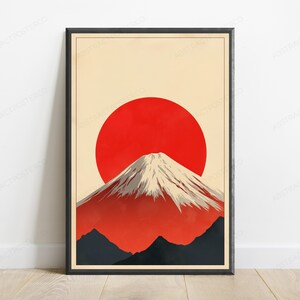 May include: A framed wall art print featuring a stylized mountain with a snow-capped peak set against a large, solid red circular sun. The background is a pale cream color, and the lower portion of the composition shows dark gray mountain silhouettes.
