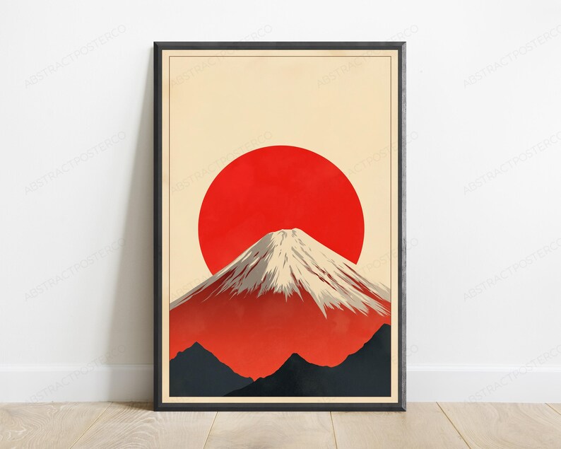 May include: A framed wall art print featuring a stylized mountain with a snow-capped peak set against a large, solid red circular sun. The background is a pale cream color, and the lower portion of the composition shows dark gray mountain silhouettes.