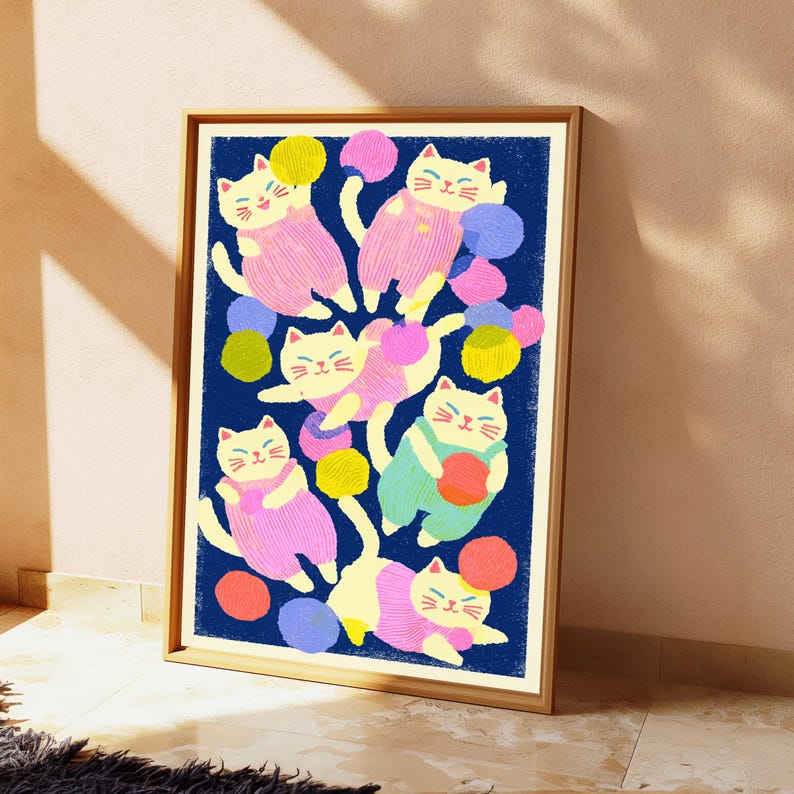 May include: A framed art print featuring a dark blue background with six white cats wearing colorful overalls. The cats are depicted playing with various round balls of yarn in shades of yellow, pink, orange, and purple, arranged in a playful pattern.