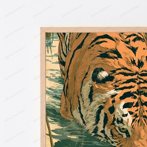 May include: A framed wall art print featuring a close-up illustration of a tiger with orange fur and black stripes wading through shallow, muted green water. The artwork is encased in a light-colored wooden frame with a clean, simple border.