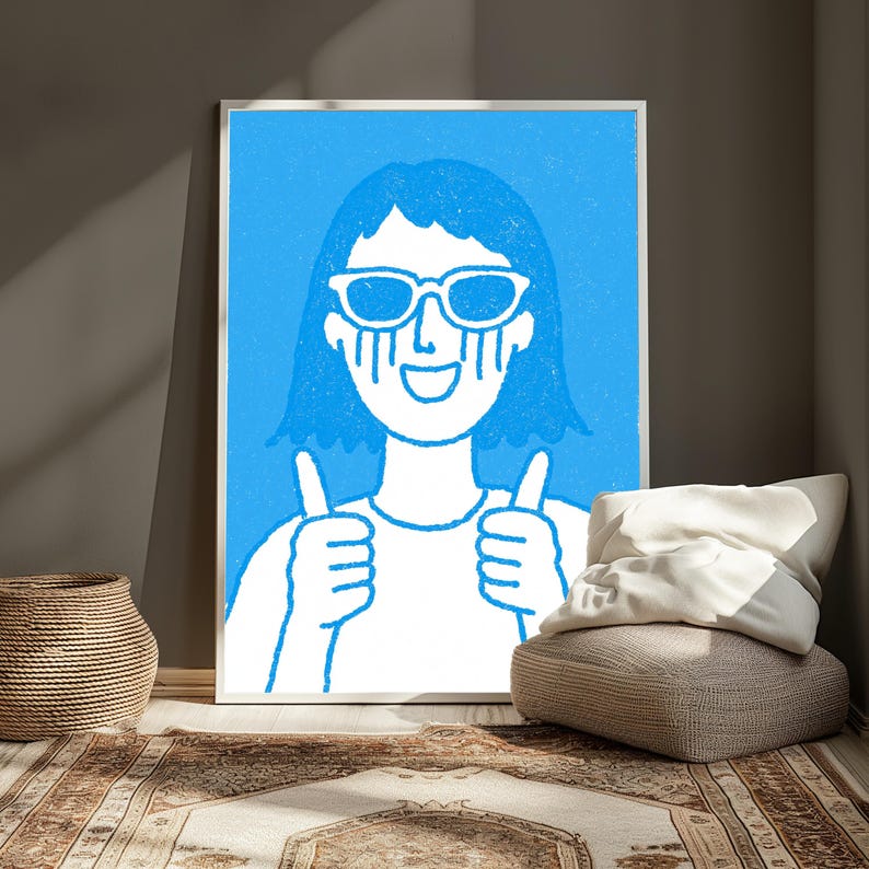 May include: A framed wall art print featuring a white line drawing of a person with short hair wearing sunglasses and smiling while giving a double thumbs up gesture, set against a solid bright blue background with a textured appearance.