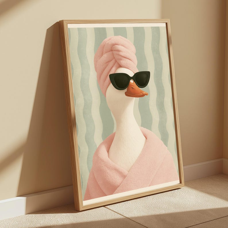 Puede incluir: Una l&aacute;mina de arte mural enmarcada que muestra un pato blanco con una toalla rosa envuelta en la cabeza, un albornoz rosa a juego y gafas de sol negras de ojo de gato. El fondo presenta rayas verticales onduladas en verde claro y blanco.