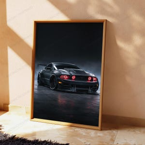 May include: A framed vertical wall art print featuring a dark grey sports car with glowing red circular headlights. The vehicle is positioned on a dark, reflective surface against a moody, shadowed background, captured in a low-angle perspective.