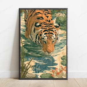 May include: A rectangular wall art print featuring an orange and black tiger wading through shallow water. The scene includes green lily pads and light orange lotus flowers. The tiger is looking downward, with its reflection visible in the water.