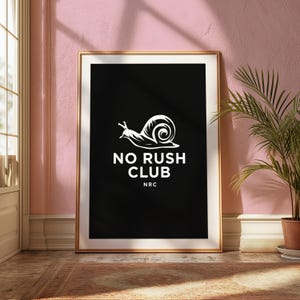 May include: A framed rectangular wall art piece featuring a black background with a white graphic of a snail. Below the snail, the text reads NO RUSH CLUB in white capital letters, followed by the smaller white text NRC centred underneath.