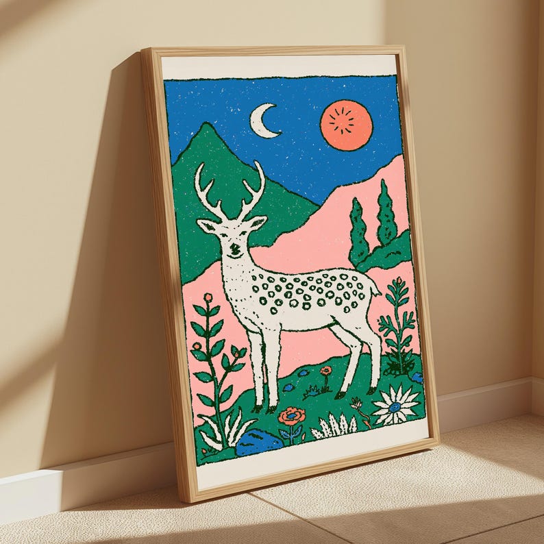 May include: A framed art print featuring a white spotted deer standing in a landscape with green mountains, a pink hillside, and a blue sky containing a white crescent moon and a red sun. The foreground includes various colorful flowers and plants.