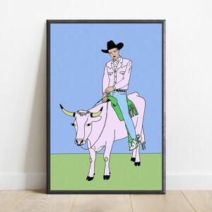 May include: A framed art print featuring a line drawing of a person in a black cowboy hat, pink jacket, and blue jeans riding a pink cow. The person wears a polka-dot shirt and spurs. The background consists of a light blue sky and green ground.