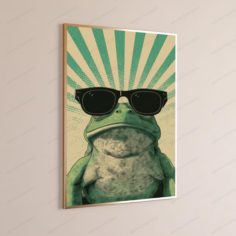 May include: A framed wall art print featuring a green frog wearing large black sunglasses. The background consists of a beige and teal sunburst pattern with a dotted texture. The frog is positioned centrally, looking forward with a neutral expression.
