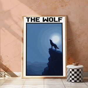 May include: A framed wall art print featuring a pixelated illustration of a wolf howling at a full moon from a rocky cliff. The text THE WOLF is printed in a bold, black, pixelated font at the top of the white-bordered rectangular poster.
