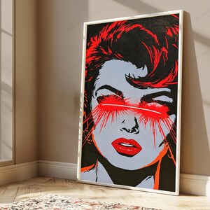 May include: A rectangular wall art print featuring a high-contrast graphic illustration of a face. The image uses a palette of black, grey, and vibrant red. A horizontal red beam of light crosses the eyes, with red streaks radiating outward.