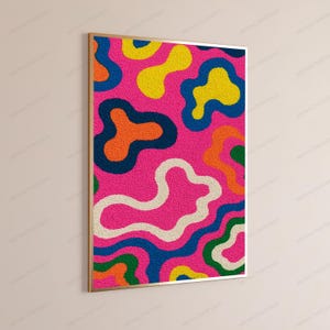 May include: A rectangular wall art piece featuring a textured, tufted surface with a vibrant pattern of organic, amoeba-like shapes in bright pink, yellow, orange, dark blue, green, and cream, all enclosed within a thin, metallic gold frame.