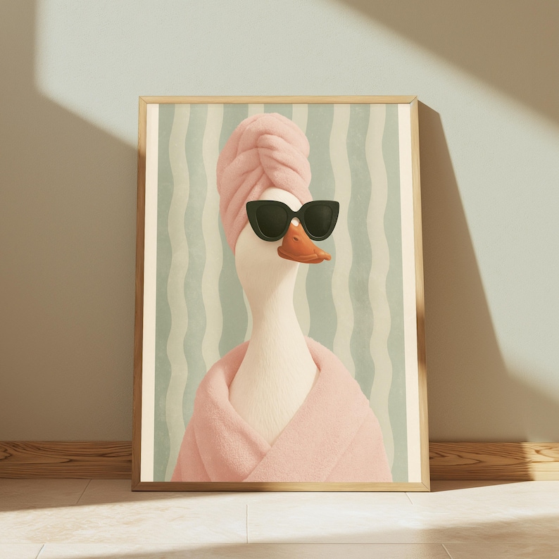 Puede incluir: Una l&aacute;mina de arte mural enmarcada que muestra a un ganso blanco con una toalla rosa envuelta en la cabeza, un albornoz rosa a juego y gafas de sol negras de ojo de gato sobre un fondo de rayas onduladas de color verde claro y blanco.
