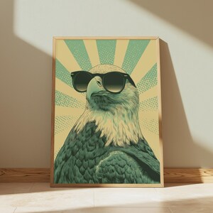 May include: A rectangular wall art print featuring a stylized illustration of a bald eagle wearing black sunglasses. The eagle is centered against a background of alternating light yellow and teal sunburst rays with a dotted texture pattern.