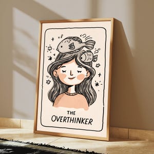 K&ouml;nnte beinhalten: Ein gerahmter Kunstdruck mit einer Strichzeichnung einer Person mit geschlossenen Augen und zwei Fischen auf dem Kopf. Der Hintergrund ist cremefarben und mit kleinen Sternen verziert. Der Text THE OVERTHINKER steht am unteren Rand.
