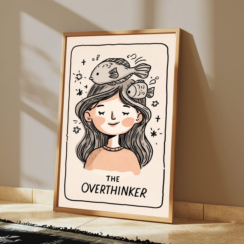 K&ouml;nnte beinhalten: Ein gerahmter Kunstdruck mit einer Strichzeichnung einer Person mit geschlossenen Augen und zwei Fischen auf dem Kopf. Der Hintergrund ist cremefarben und mit kleinen Sternen verziert. Der Text THE OVERTHINKER steht am unteren Rand.