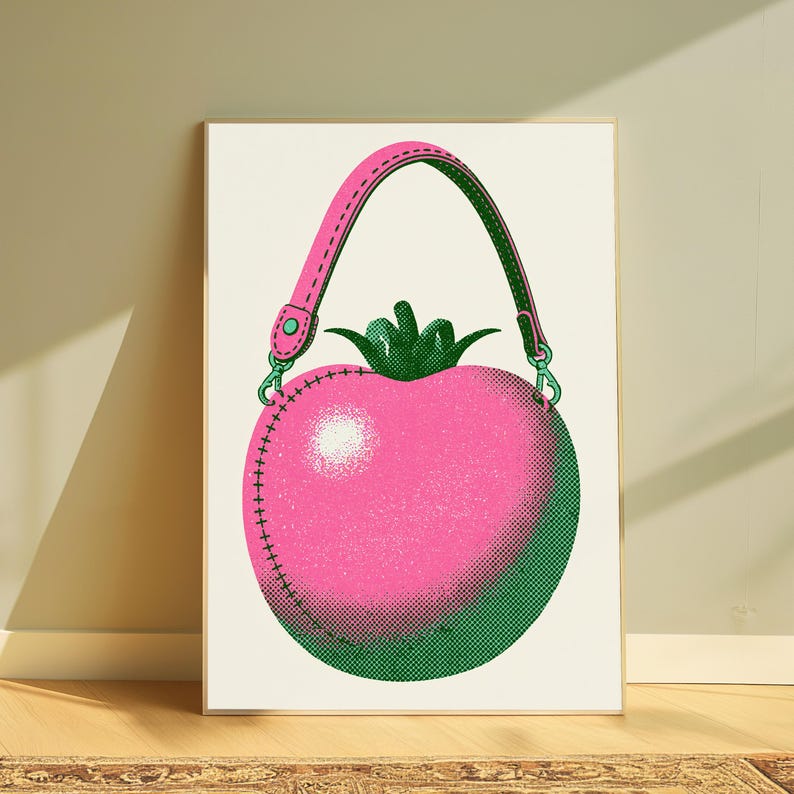 May include: A framed art print featuring a stylized illustration of a round, pink tomato-shaped handbag. The design includes a pink strap with green accents, a green stem at the top, and a dotted halftone texture throughout the artwork.