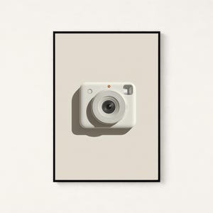 May include: A framed wall art print featuring a centered, off-white instant camera with a prominent circular lens, a small orange dot above the lens, and a rectangular viewfinder, set against a solid light beige background within a thin black frame.