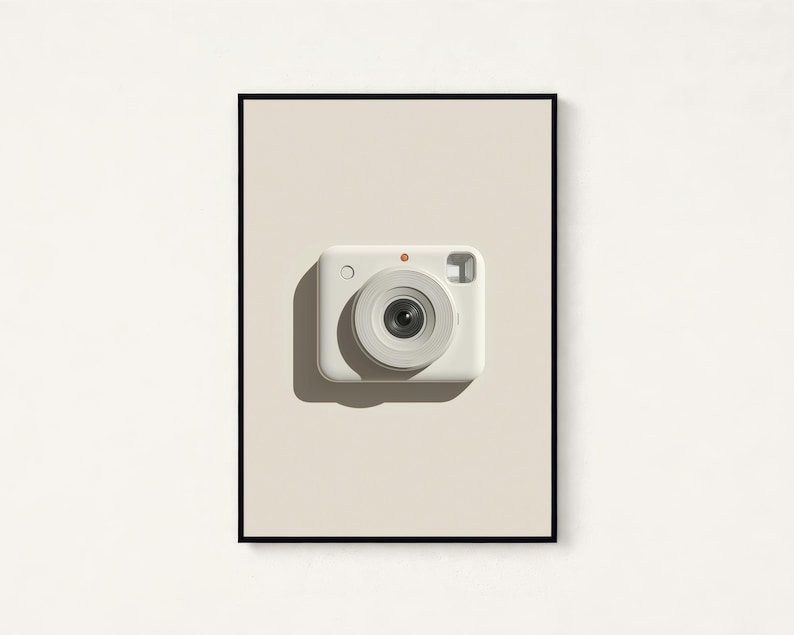May include: A framed wall art print featuring a centered, off-white instant camera with a prominent circular lens, a small orange dot above the lens, and a rectangular viewfinder, set against a solid light beige background within a thin black frame.