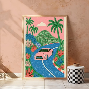 May include: A framed art print featuring a pink sports car driving along a winding blue road. The scene includes green palm trees, textured green hills, and vibrant red and blue foliage against a solid pink sky with a single white cloud.