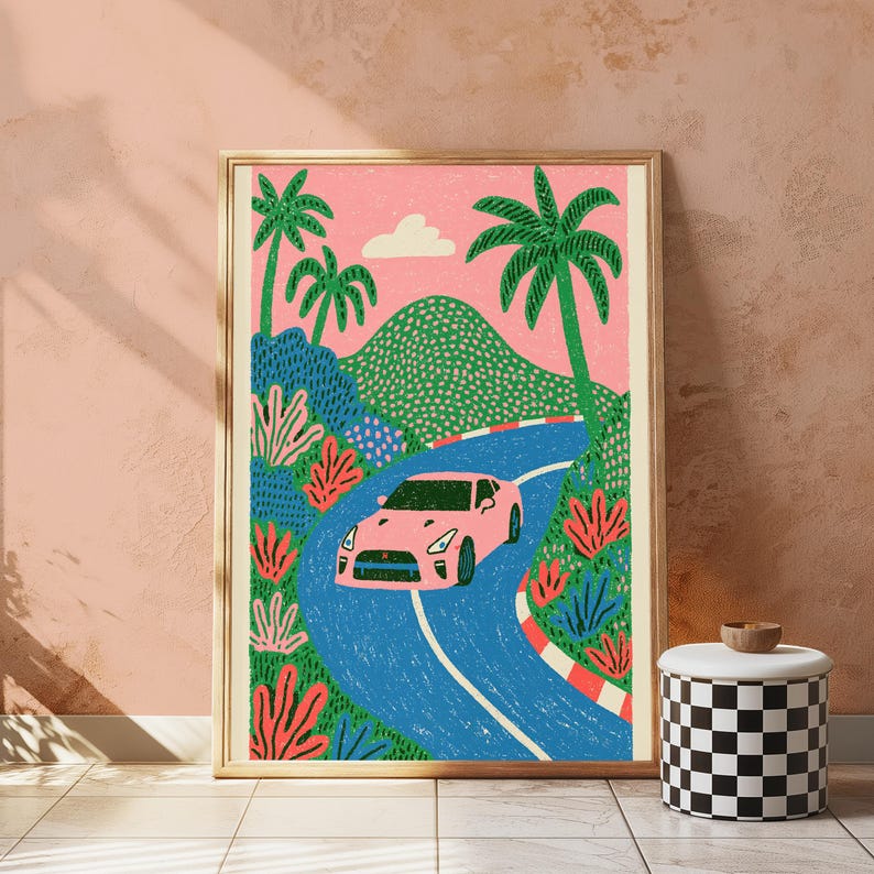 May include: A framed art print featuring a pink sports car driving along a winding blue road. The scene includes green palm trees, textured green hills, and vibrant red and blue foliage against a solid pink sky with a single white cloud.
