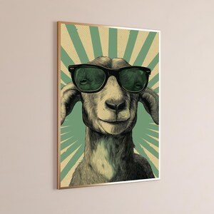 May include: A framed wall art print featuring a detailed illustration of a goat wearing black-rimmed sunglasses. The goat is centred against a background of radiating light green and cream-coloured sunburst rays with a subtle dot pattern.