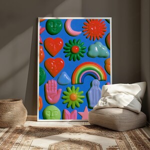 May include: A rectangular wall art print featuring a vibrant blue background covered in a repeating pattern of glossy, raised-relief icons including red hearts with faces, green suns, a rainbow, a pink hand, a light blue cloud, and a crescent moon.